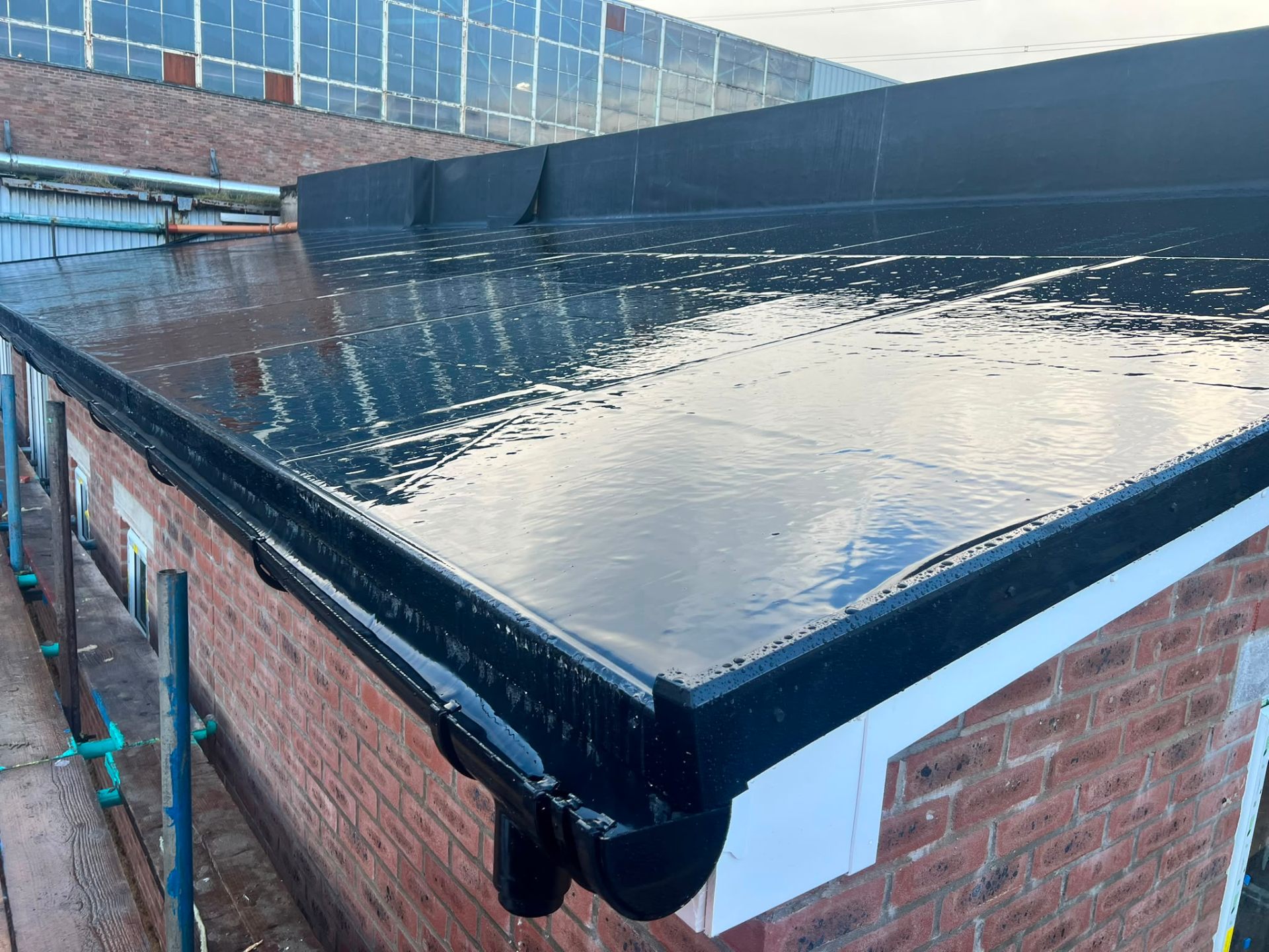 Newly installed black flat roof system on a brick extension with full guttering