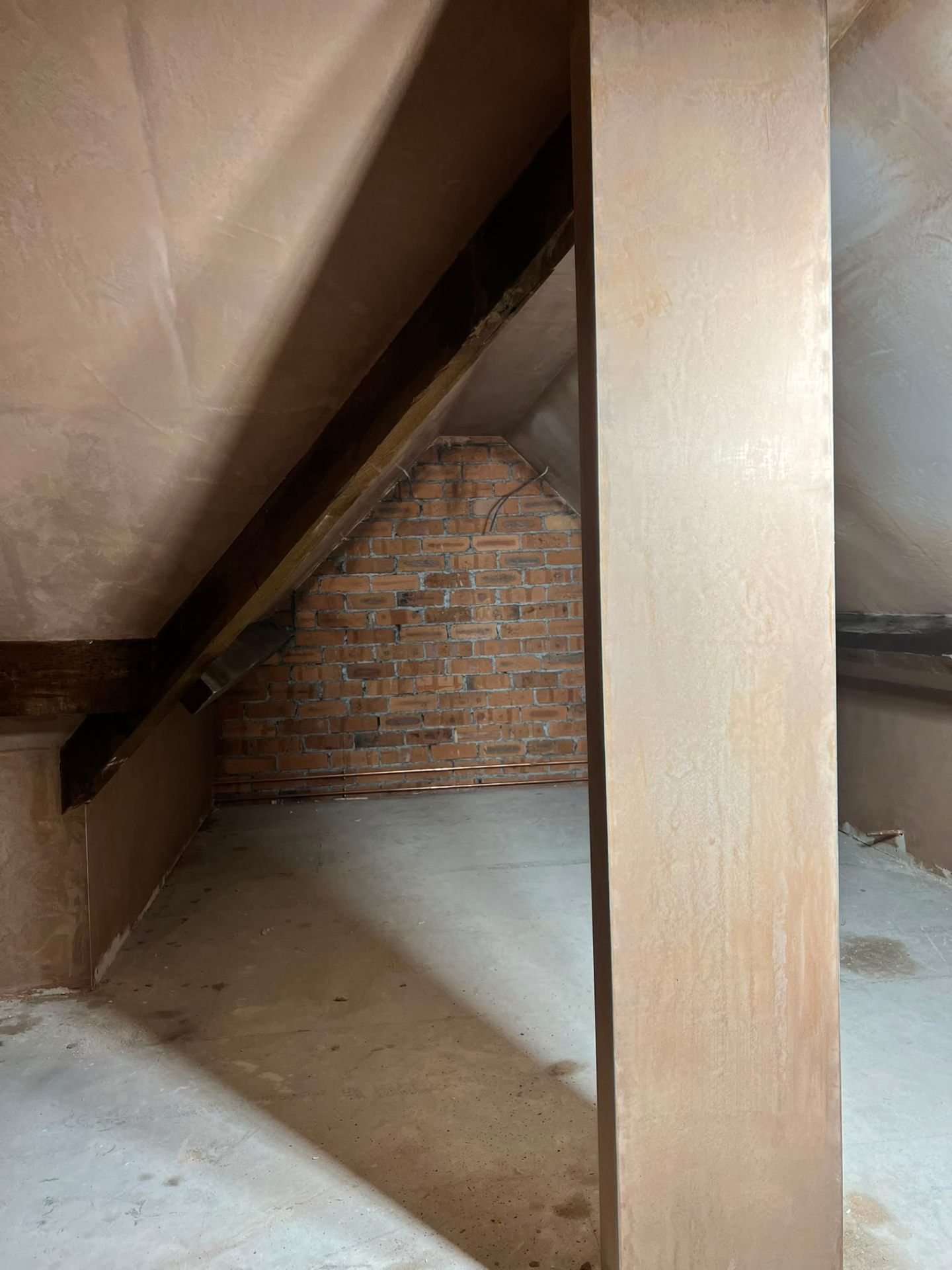 Loft conversion space in progress with plastered sloped ceilings and exposed brick internal gable wall.