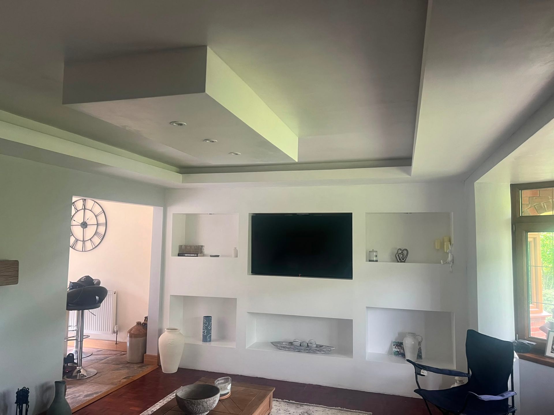 Finished modern white media wall with integrated shelving, inset television and recessed ceiling lighting