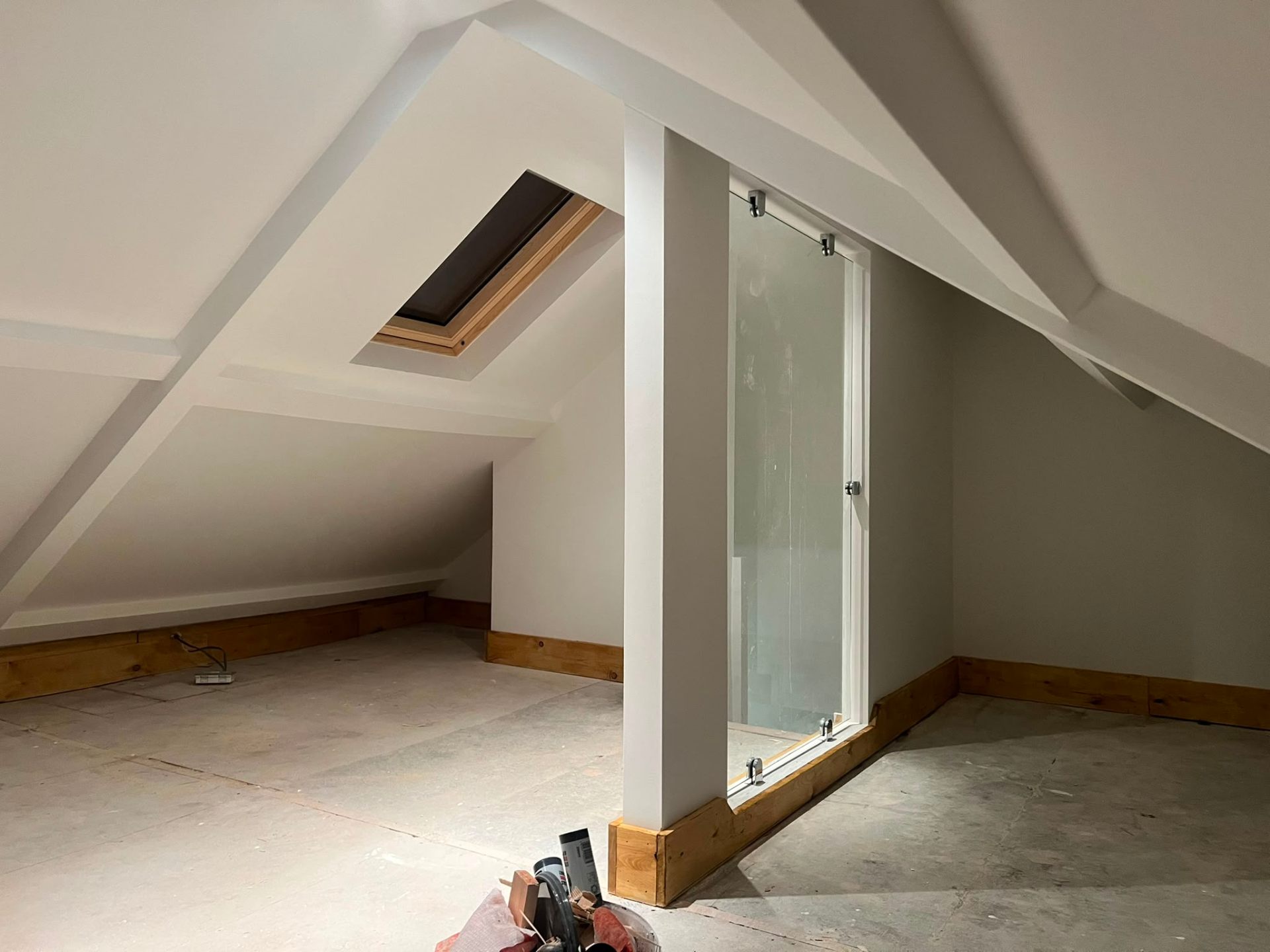 Loft conversion interior featuring a glass partition wall and skylight window in a sloped ceiling.