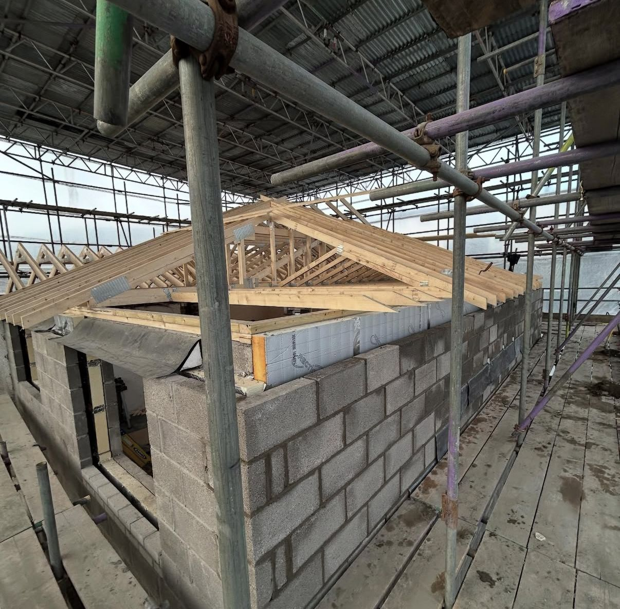 Rear extension under construction with new blockwork walls and prefabricated timber roof trusses installed beneath scaffolding.