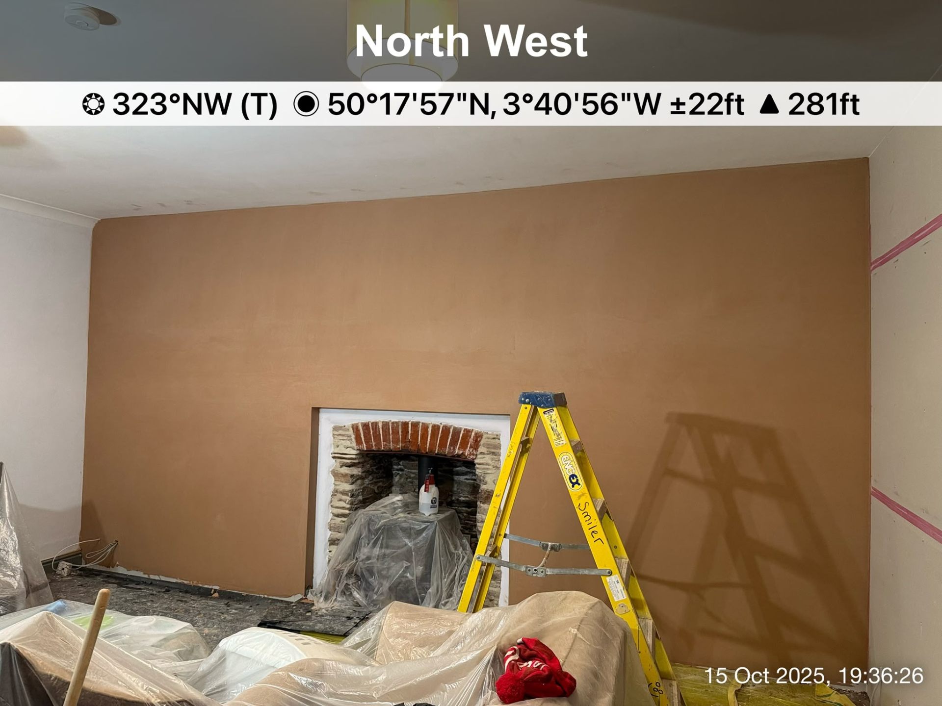 Freshly plastered interior wall with a brick fireplace opening and yellow step ladder in foreground.