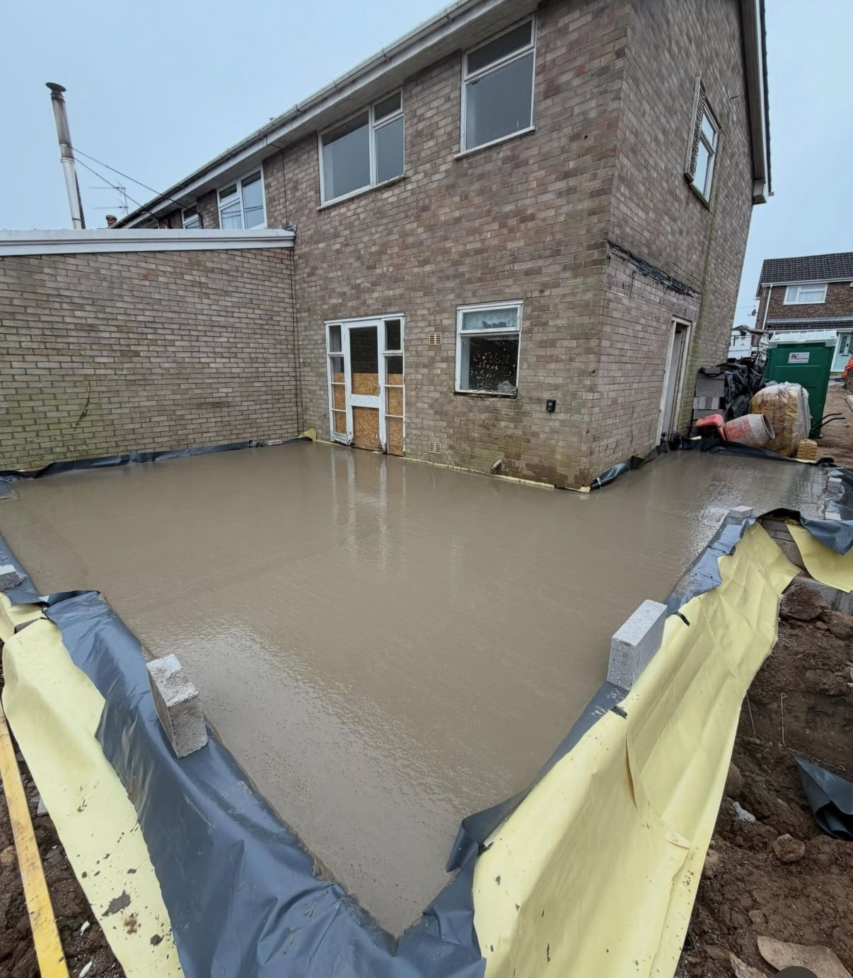 Freshly poured concrete slab for a rear extension, levelled and tamped within the blockwork foundation walls.