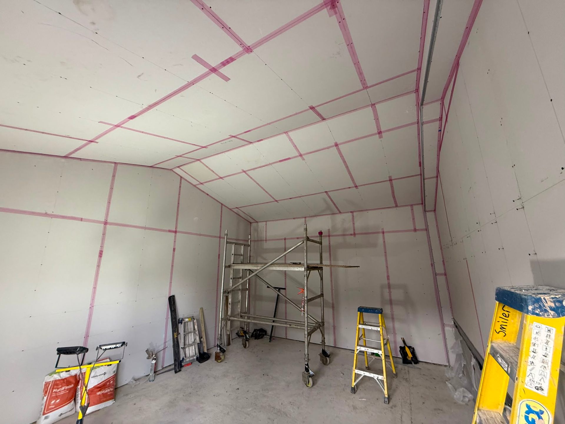 Large interior room with newly installed plasterboard and pink jointing tape on walls and ceiling