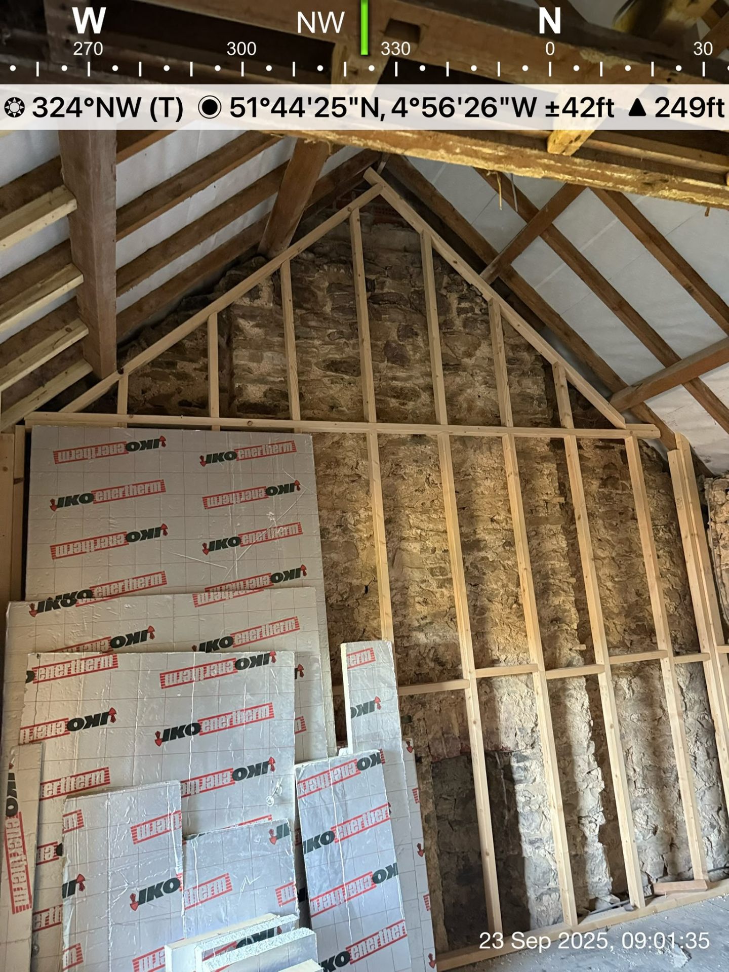 Wooden stud wall framing against a stone wall with insulation boards ready for installation.