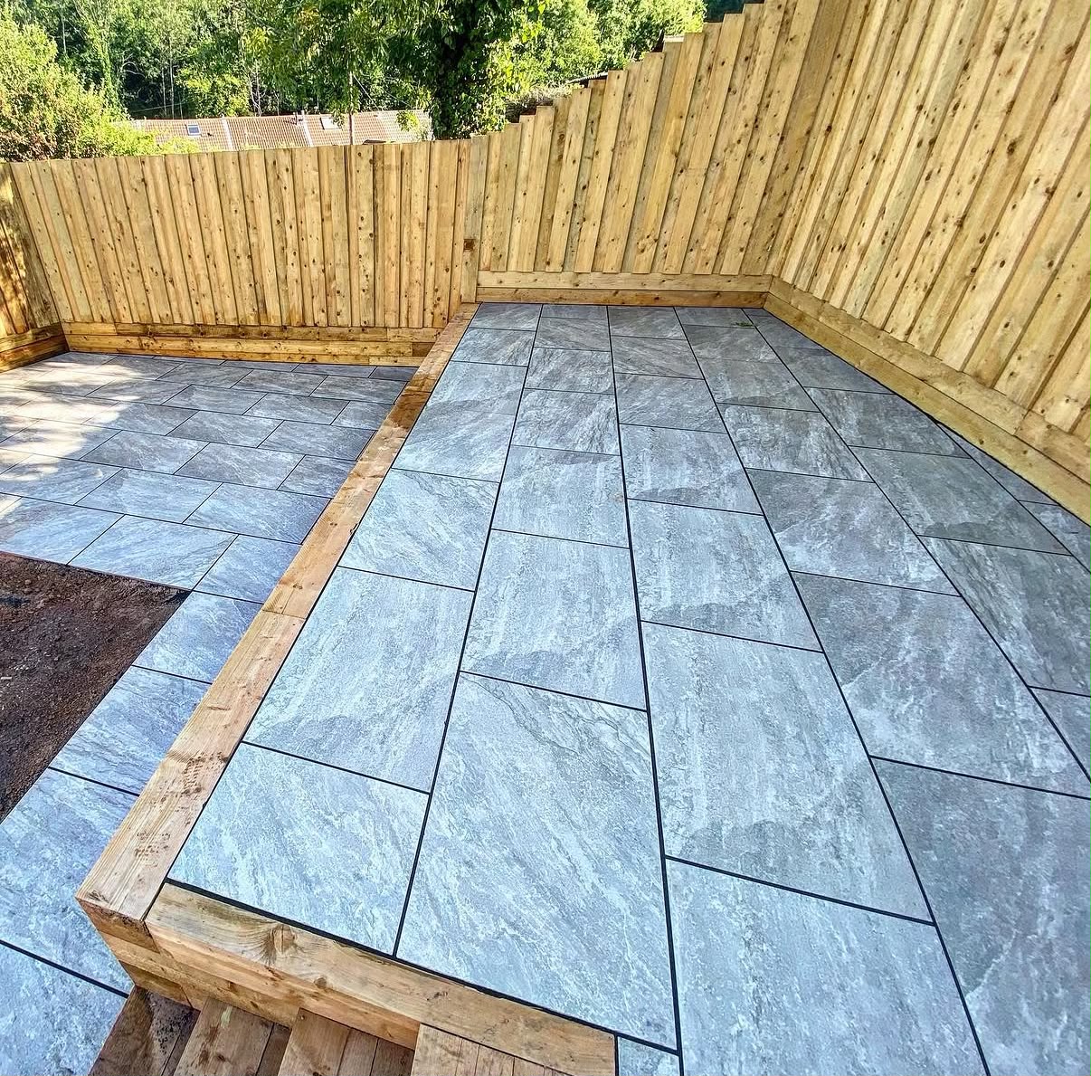 Newly laid grey stone patio with timber edging and a new privacy fence in a South Wales garden