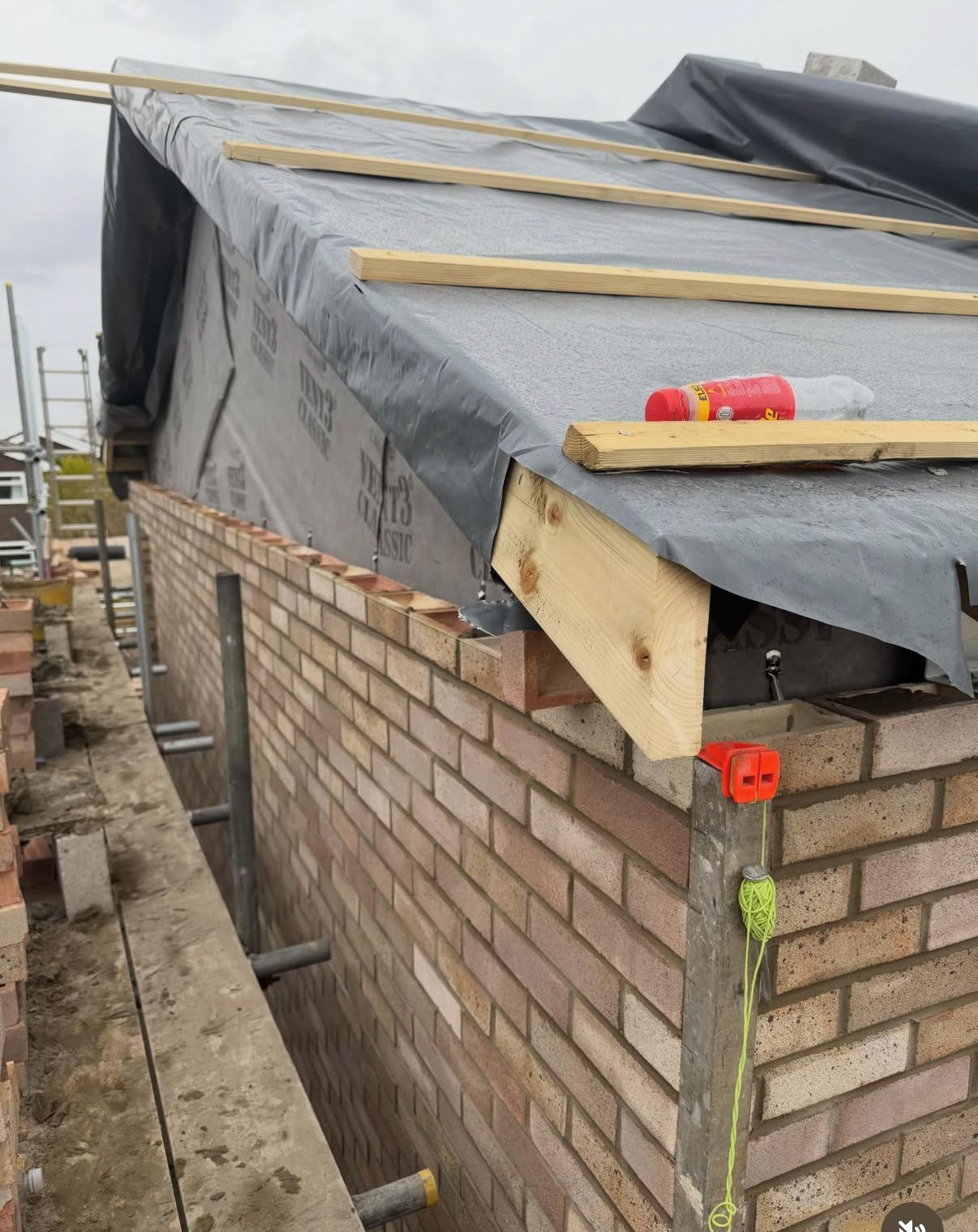 Close-up of a pitched extension roof being formed above fresh facing brickwork on a new build-up wall.