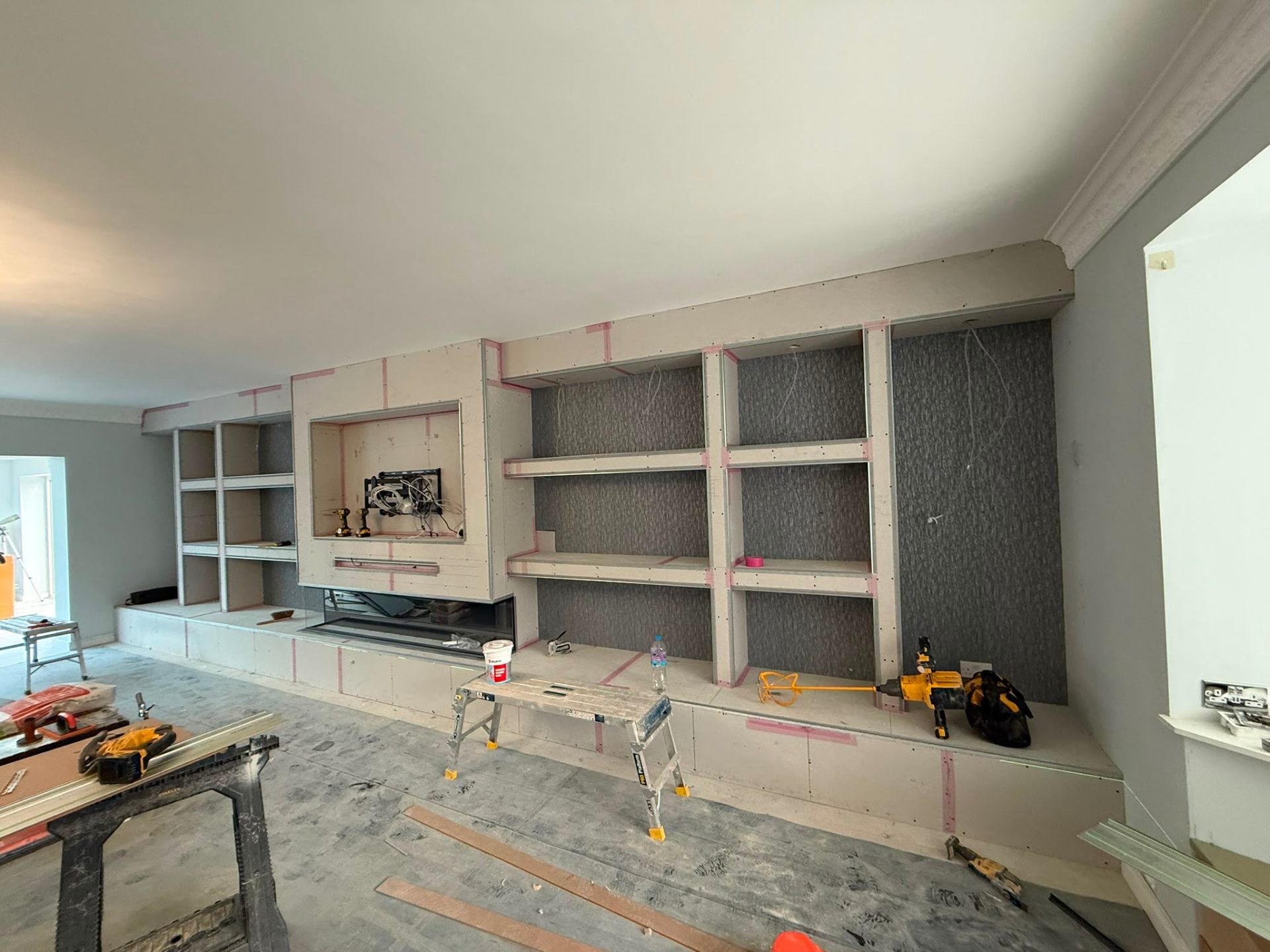 Interior view of a bespoke media wall being constructed with plasterboard and shelving units.