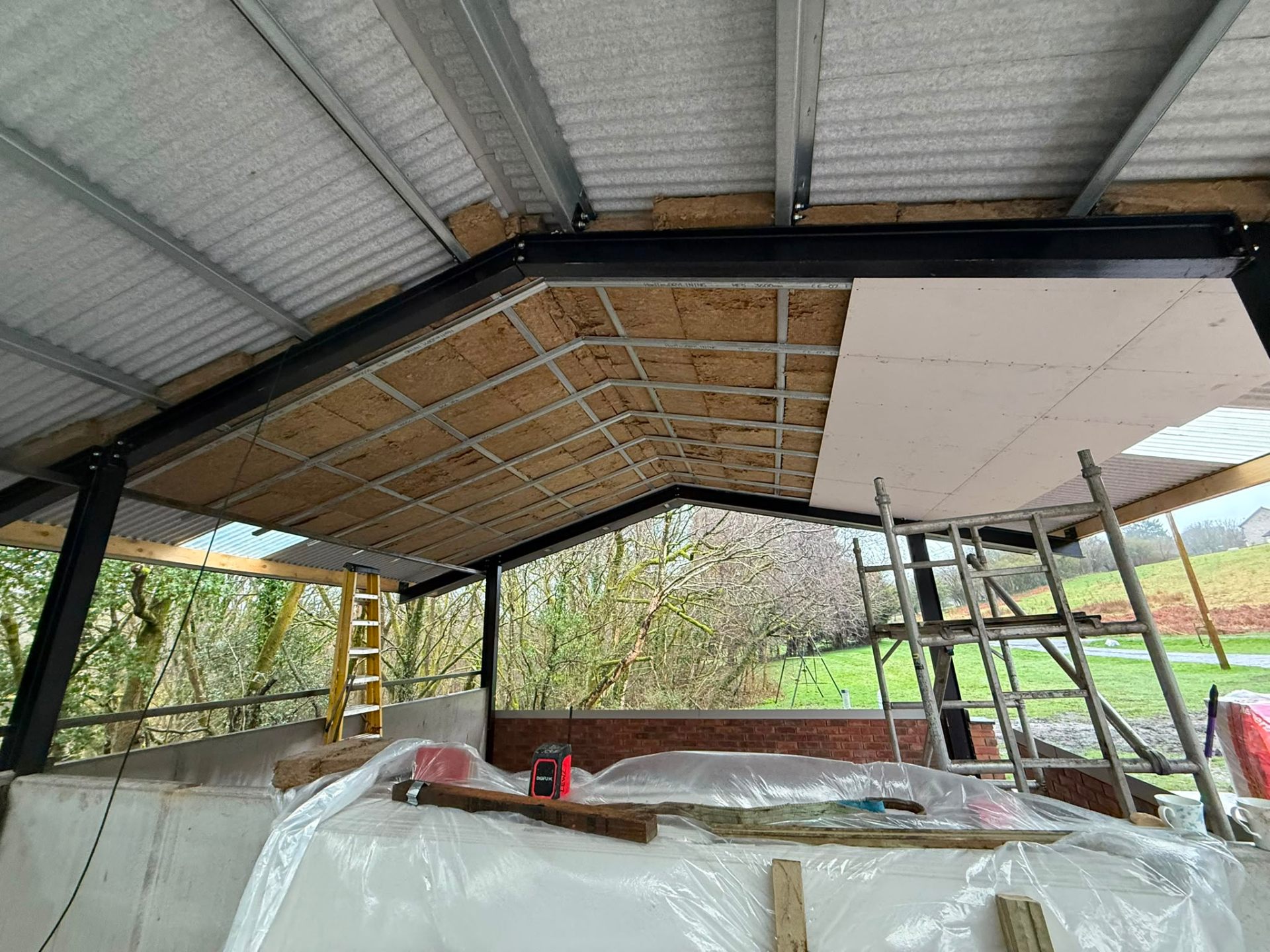 Internal view of a steel roof frame being insulated and boarded with plasterboard.