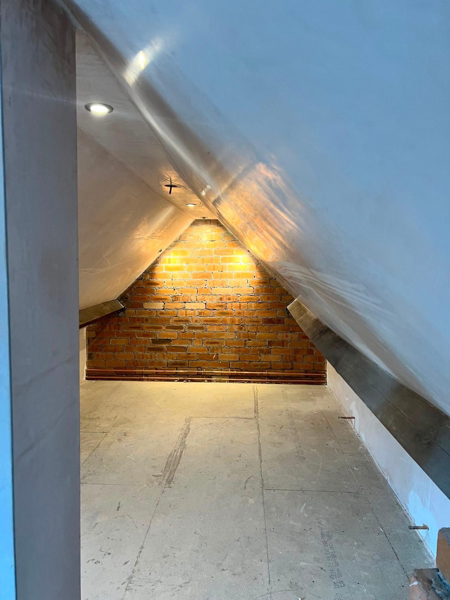 Finished loft conversion with exposed feature brick wall, warm spotlights and plastered sloping ceilings