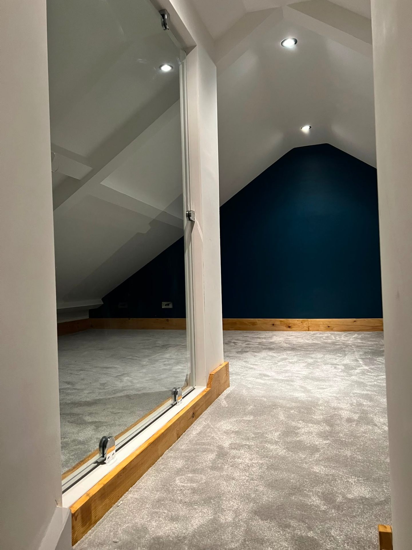 Finished loft conversion featuring plush grey carpet, glass partition and navy feature wall by LEWZ