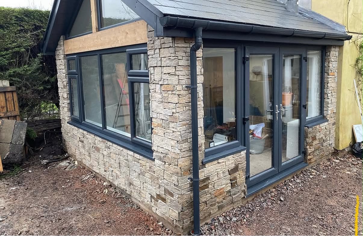 Finished single-storey extension with natural stone cladding and dark grey aluminium windows