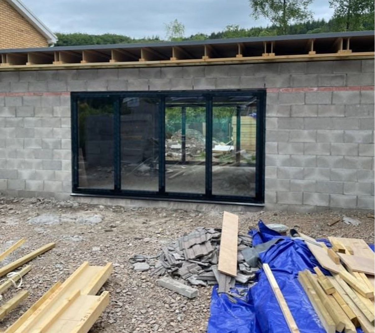 Single-storey extension shell in blockwork with newly installed aluminium bi-fold doors and timber roof joists overhead.