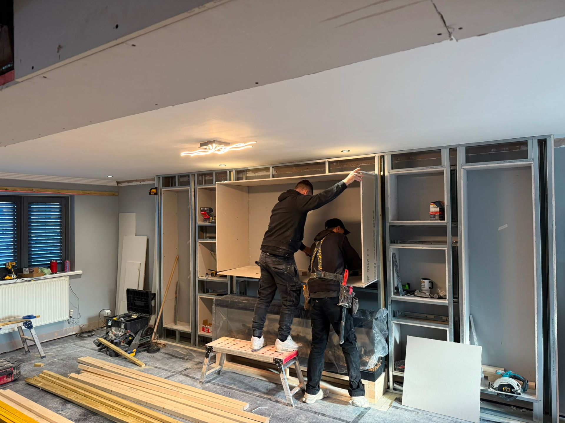 Contractors installing plasterboard onto a metal stud frame for a custom media wall unit.