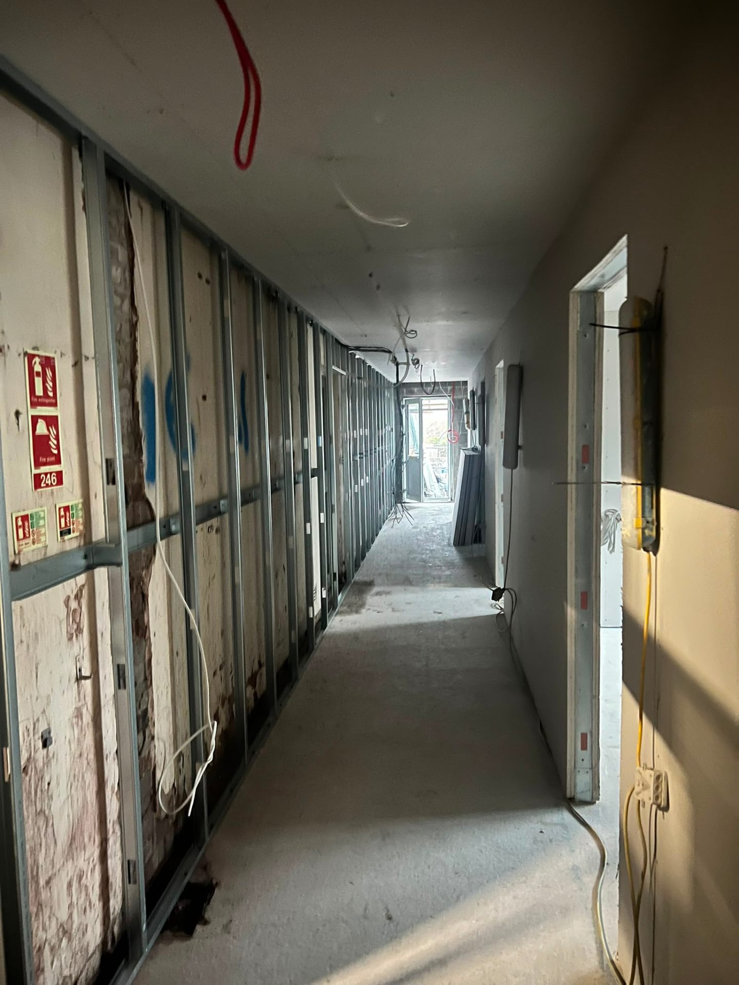 Long interior corridor showing metal stud wall partitioning framing and exposed wiring during construction