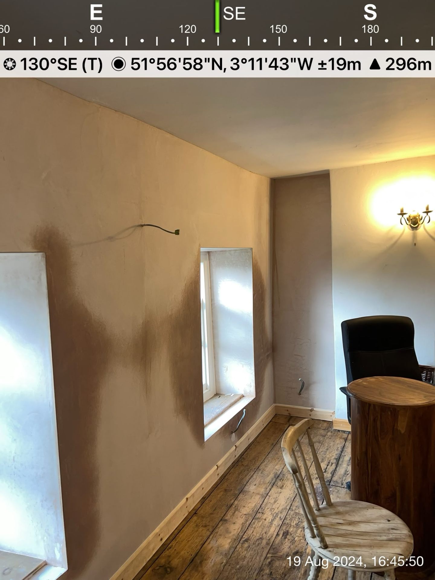Interior room with patchy fresh plaster on walls around windows and wooden floorboards.