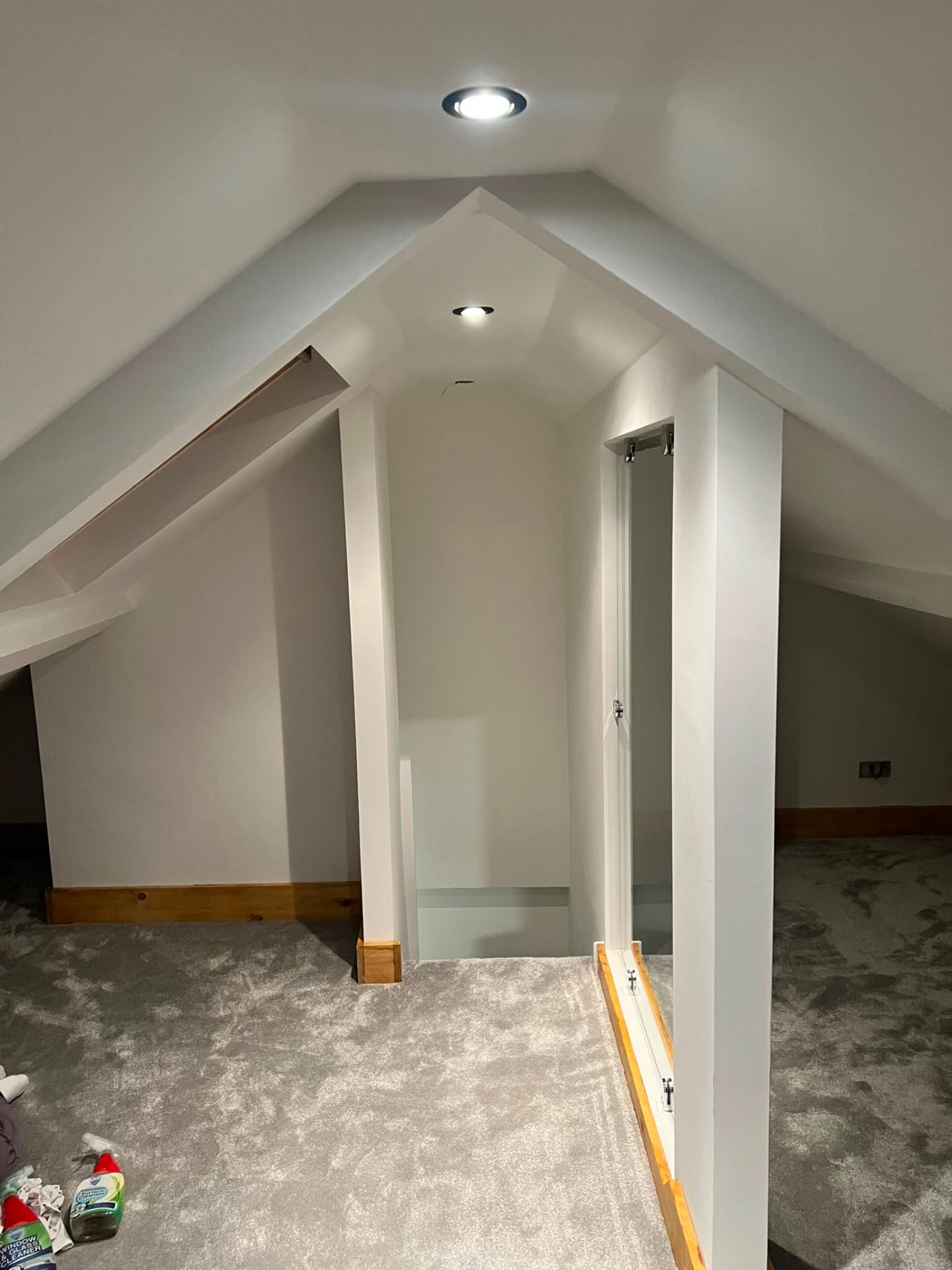 A completed attic conversion featuring grey carpets, white painted walls, and recessed ceiling spotlights.
