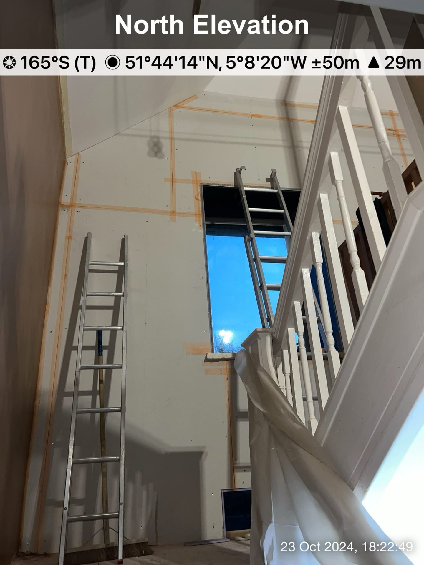 Interior stairwell under construction with new plasterboard sheets installed and ladders present.